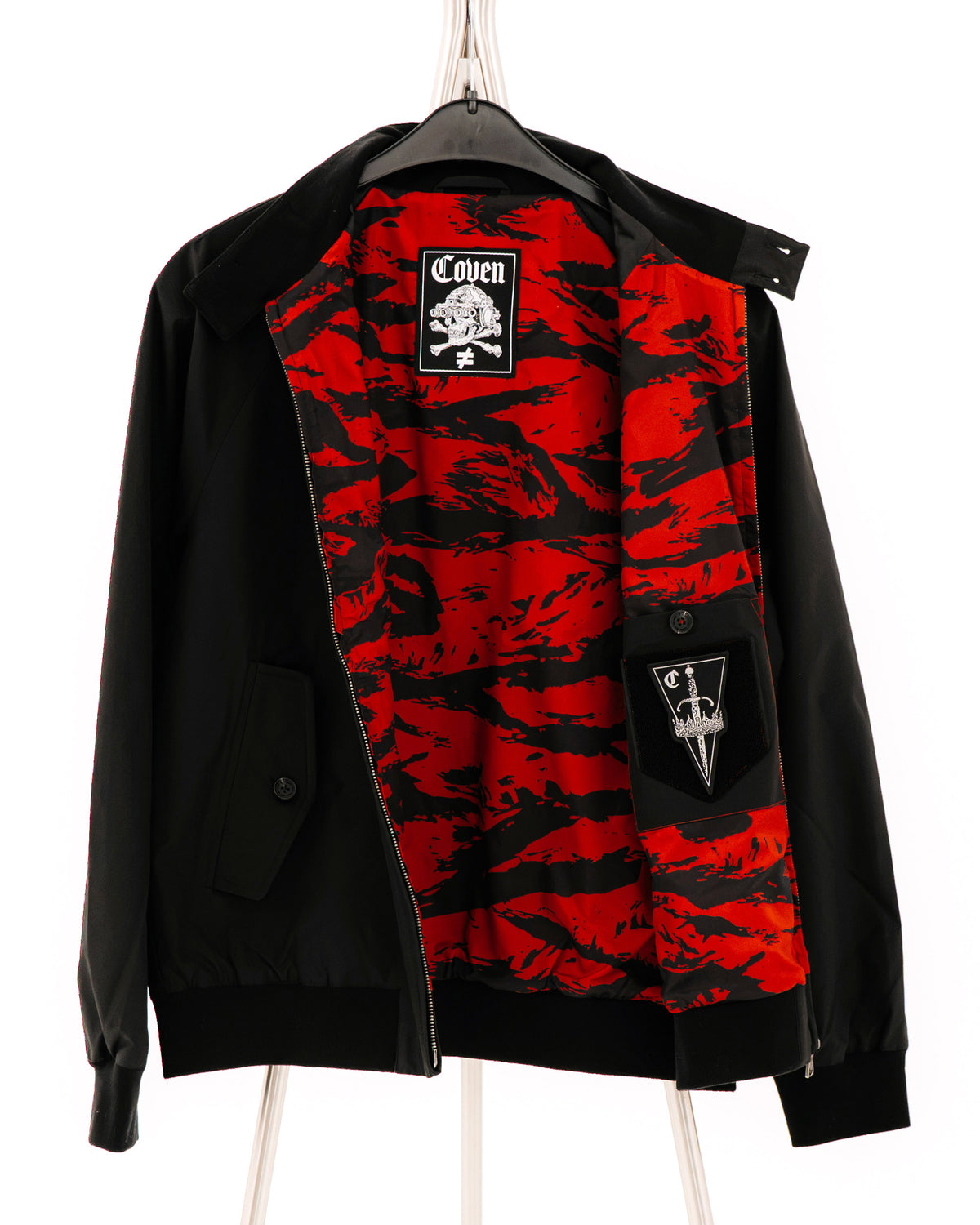 The Pariah Harrington Jacke in Schwarz, geöffnet am Bügel in Dreiviertelansicht mit Tiger Stripe Red Futter