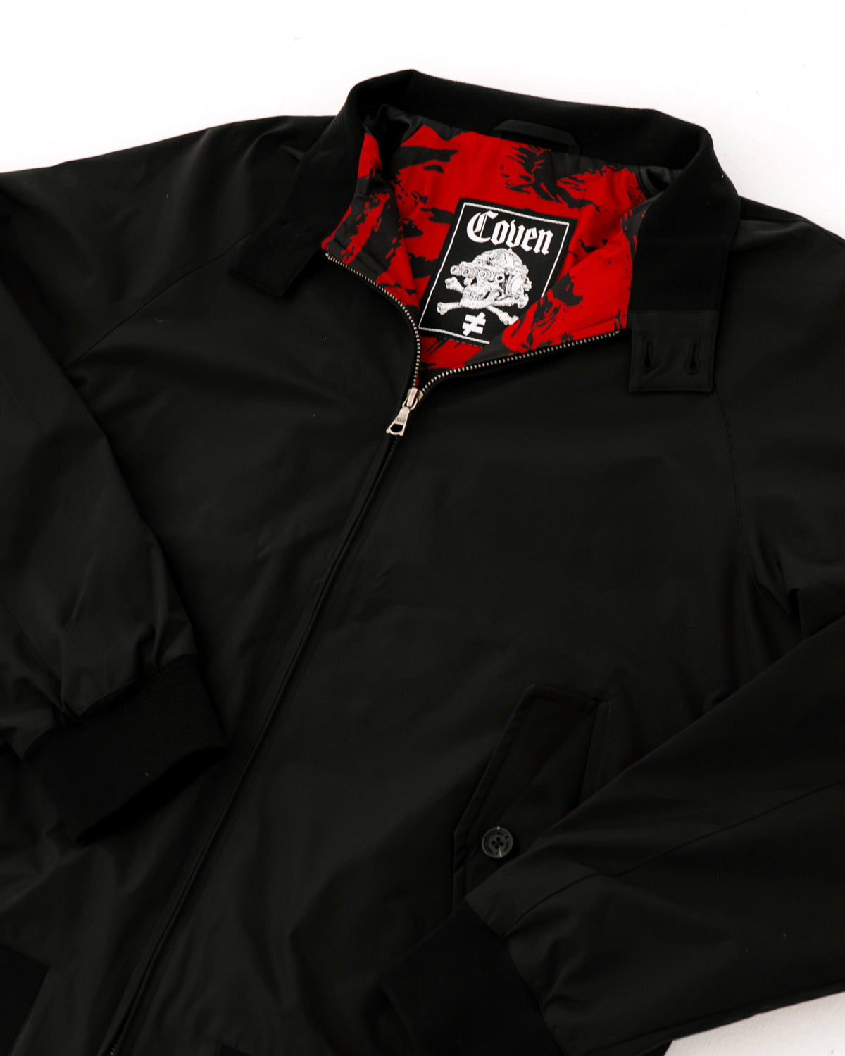 The Pariah Harrington Jacke in Schwarz, flach in Schrägansicht mit Kragen und COVEN Label