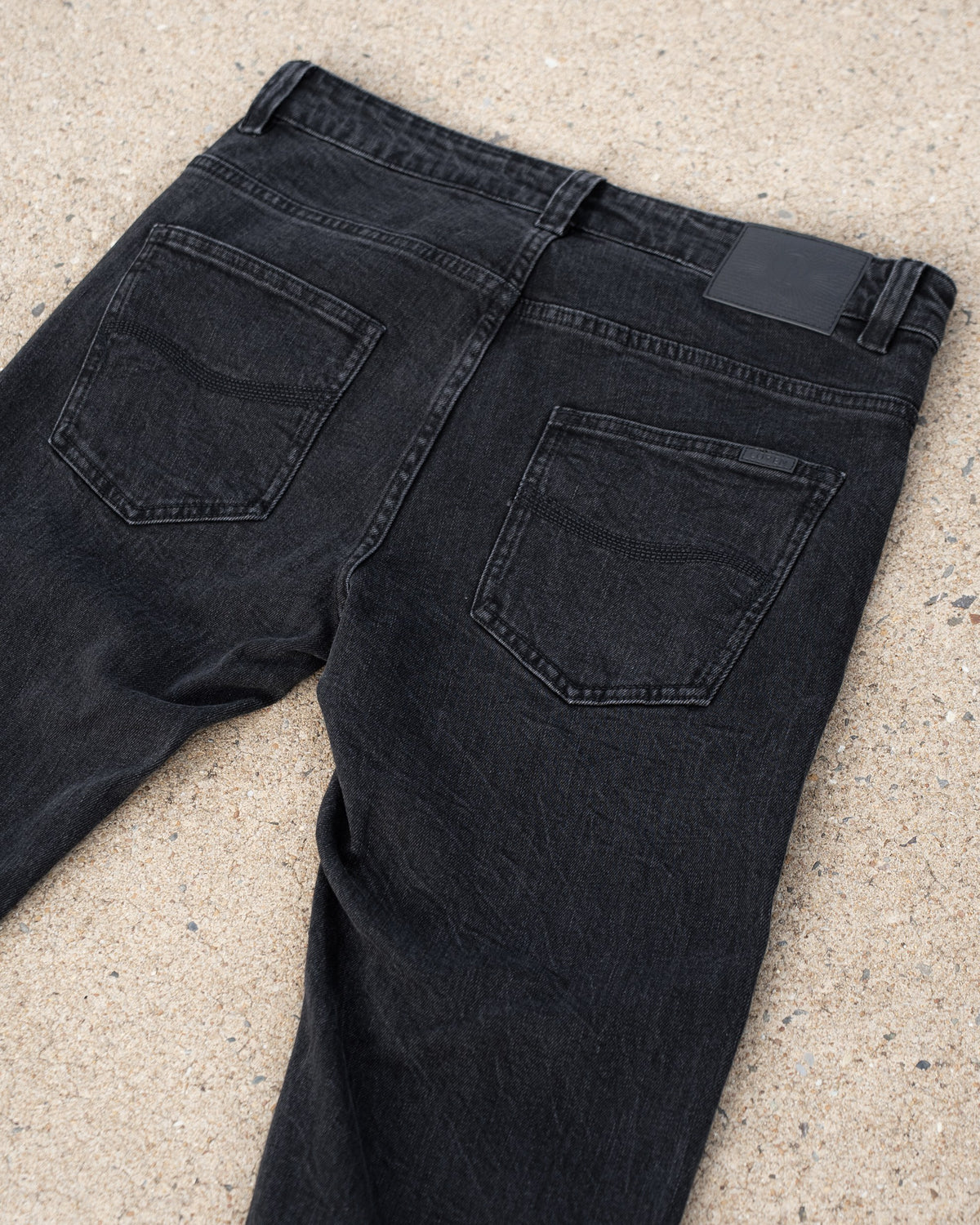 The Wormskin Jeans in Washed Black, Rückansicht schräg mit beiden Gesäßtaschen und Lederpatch
