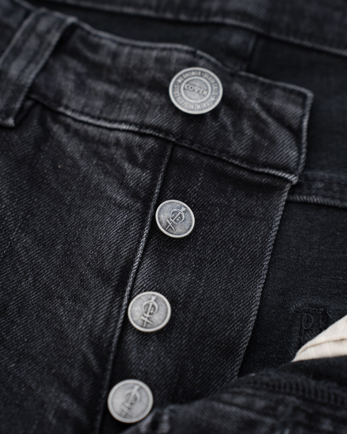 The Wormskin Jeans in Washed Black, Knopfleiste im Makro mit vier geprägten COVEN Knöpfen