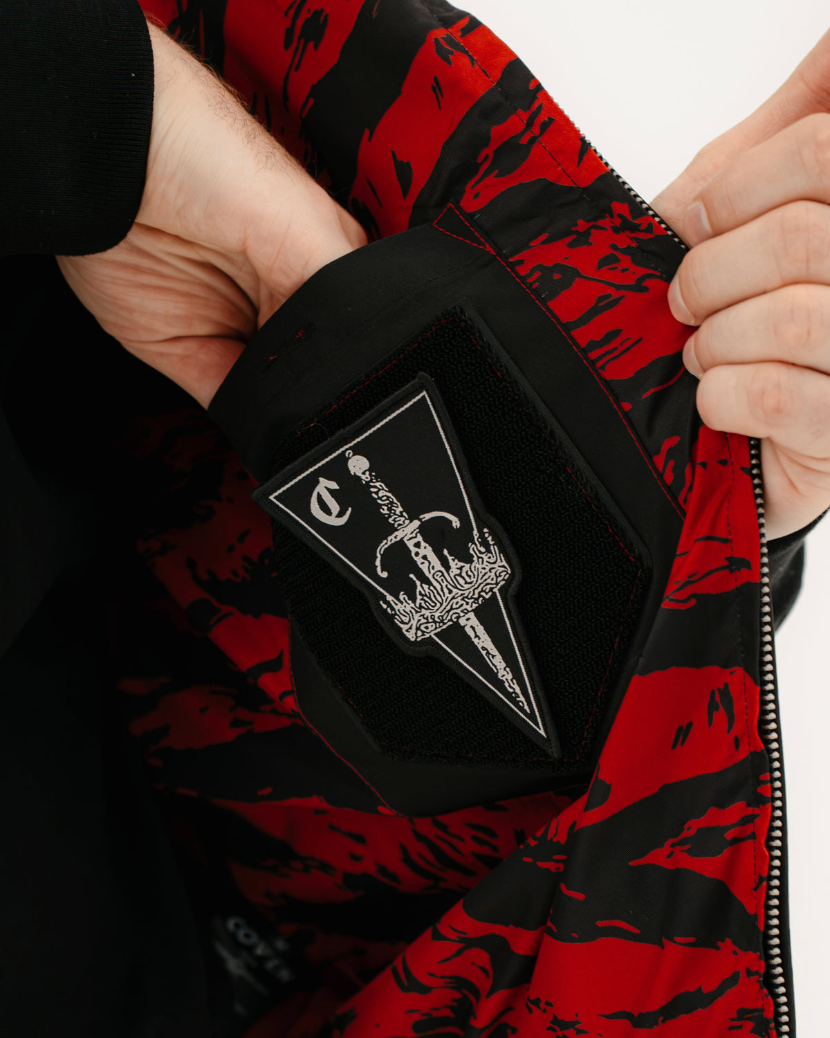 The Pariah Harrington Jacke in Schwarz am Model, COVEN Patch in der Hand vor dem Tiger Stripe Red Futter