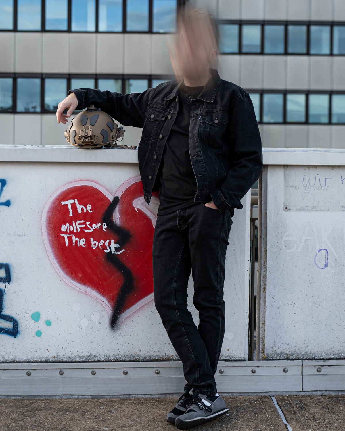 The Wormskin Jeans getragen zur Denim-Jacke, Ganzkörper vor Graffiti-Wand mit Helm in der Hand