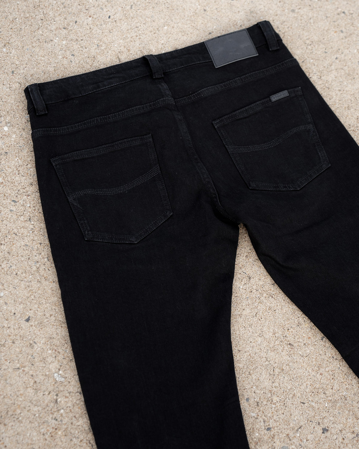 The Wormskin Jeans in Schwarz, Rückansicht flach mit ausgestellten Beinen, Gesäßtaschen und Lederpatch