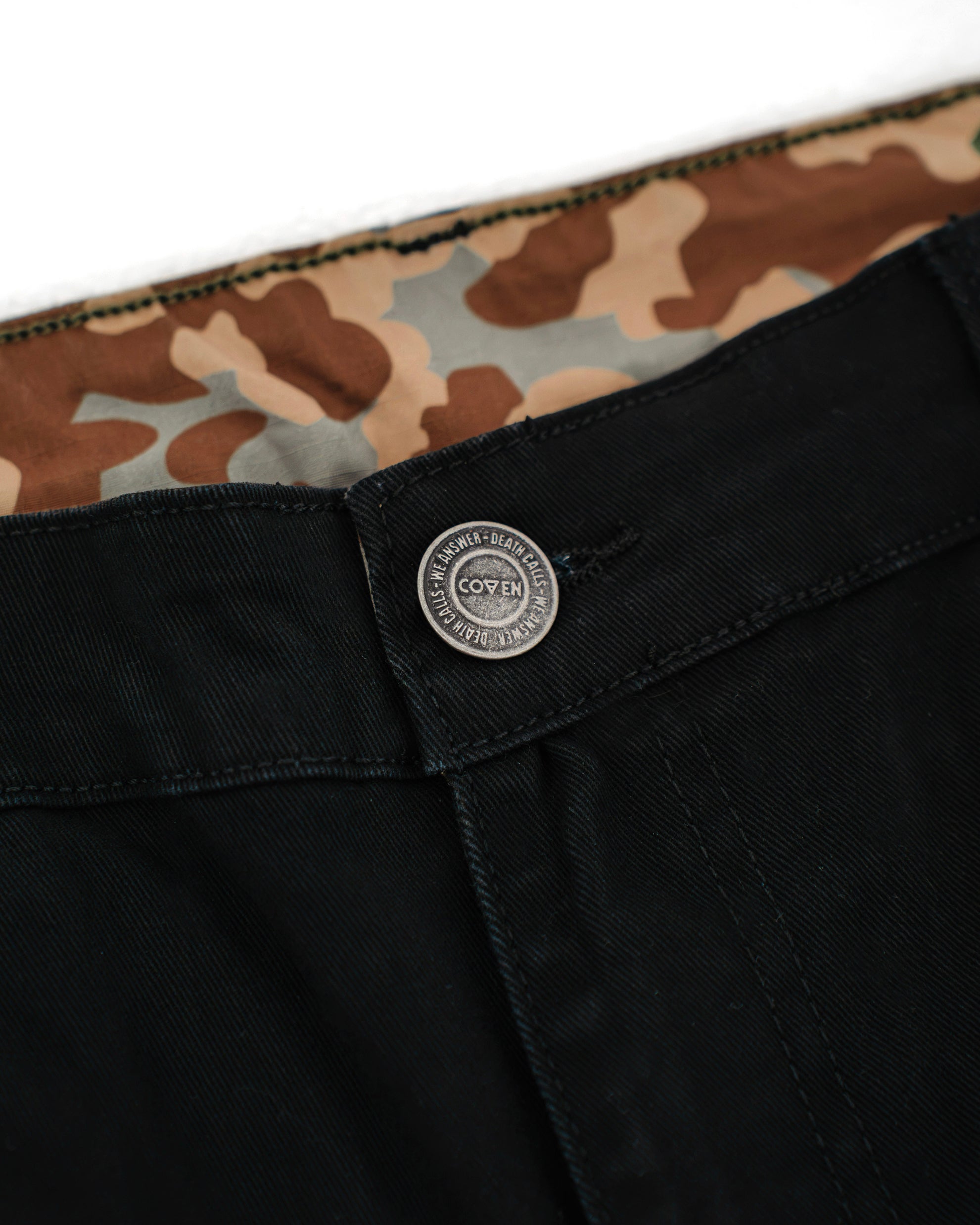Dead Drop Chino Aeon Coven Camo in Schwarz, Bunddetail mit COVEN Metallknopf und Coven-Camo-Innenfutter