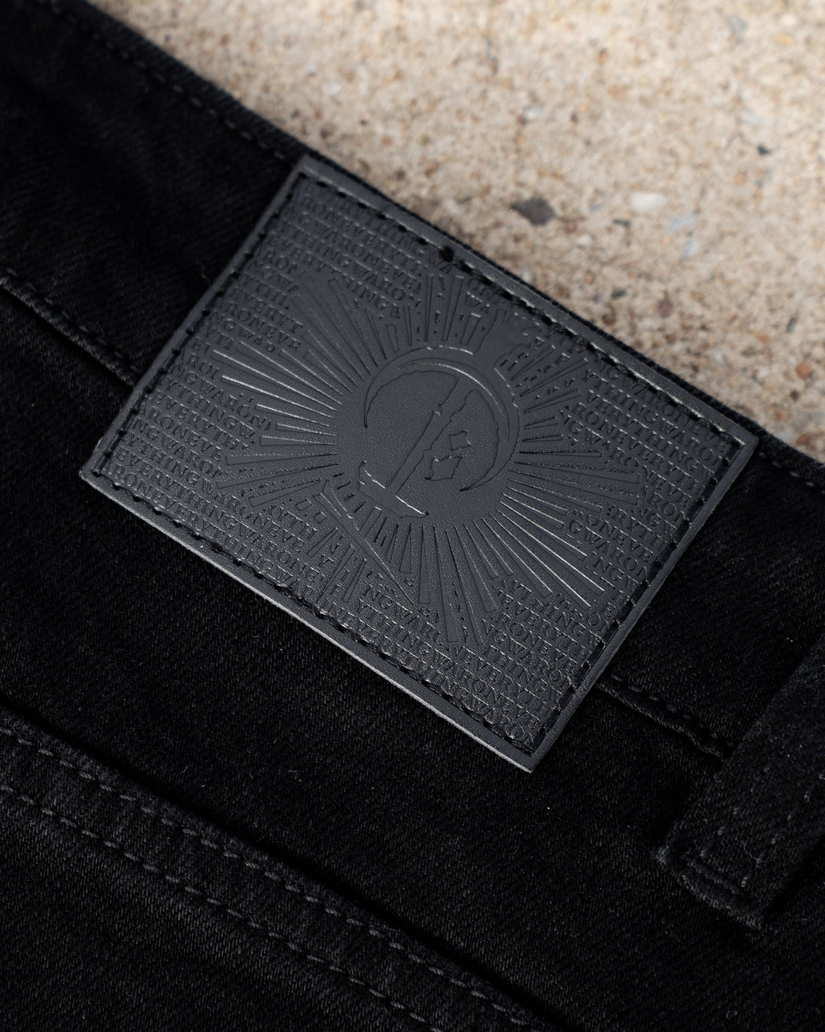 The Wormskin Jeans in Schwarz, Lederpatch am Bund im Makro mit geprägtem COVEN Strahlenkranz
