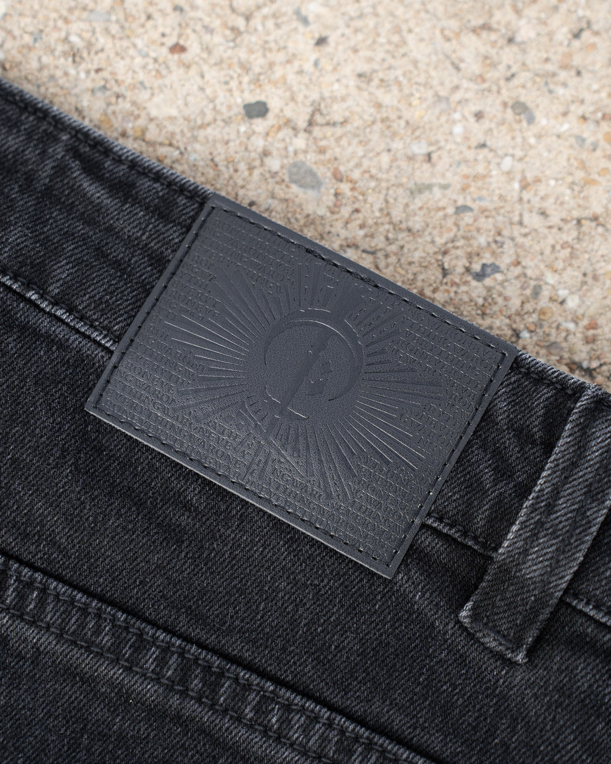 The Wormskin Jeans in Washed Black, Lederpatch am Bund im Makro mit geprägtem COVEN Strahlenkranz
