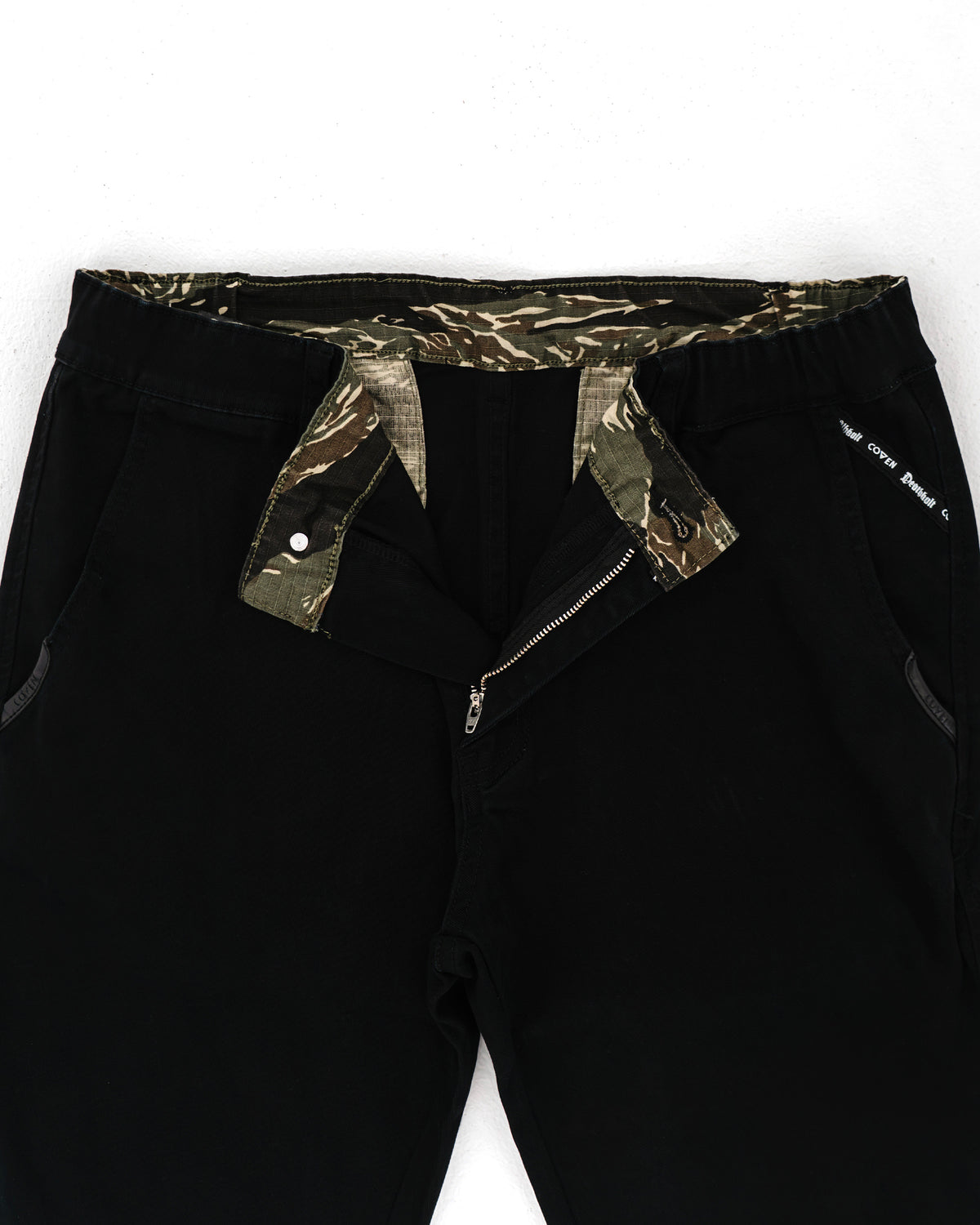 Dead Drop Chino Aeon Tigerstripe in Schwarz, geöffneter Bund mit Tigerstripe-Innenfutter und Knopfleiste