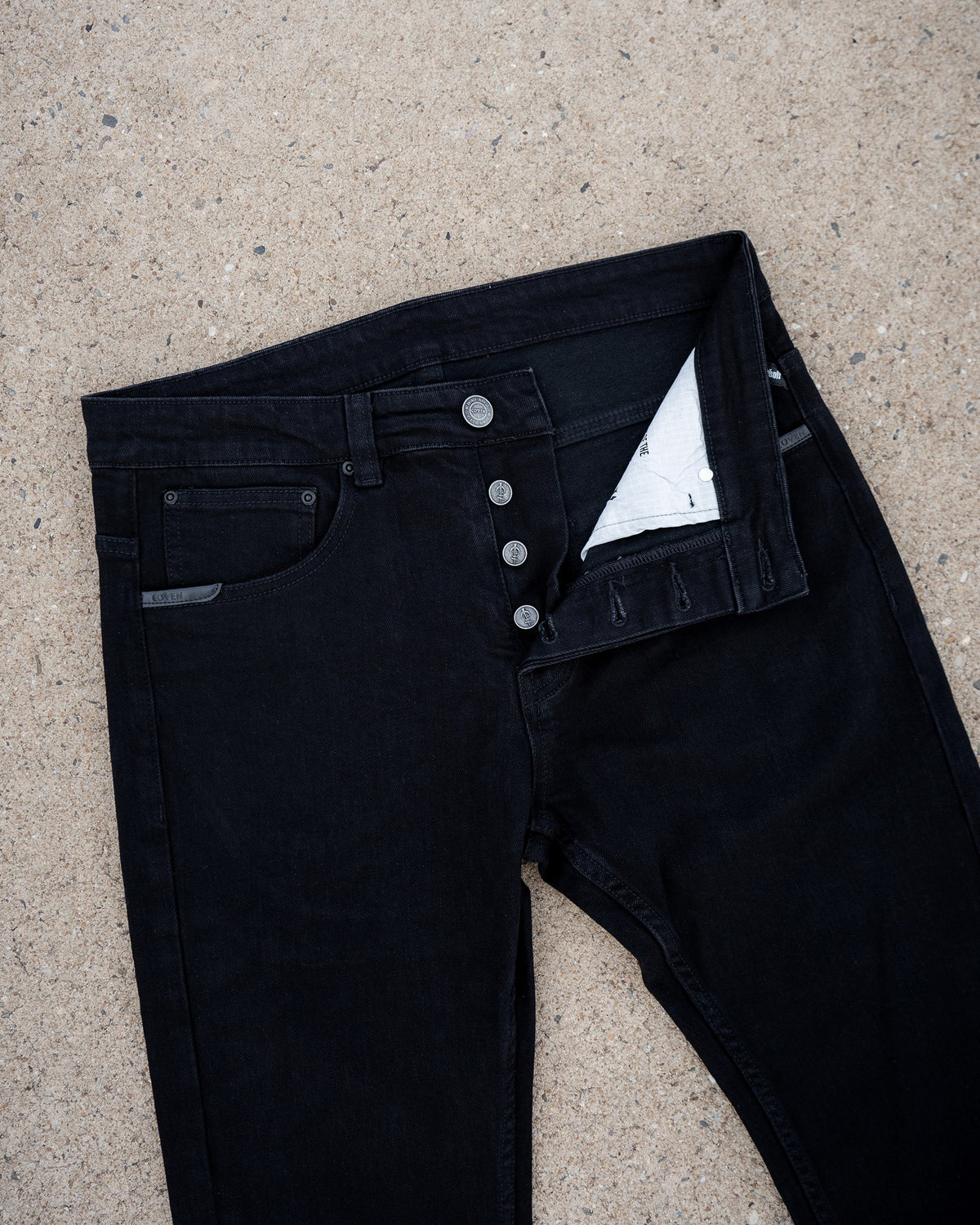 The Wormskin Jeans in Schwarz, Jeans flach von vorn mit geöffneter Knopfleiste