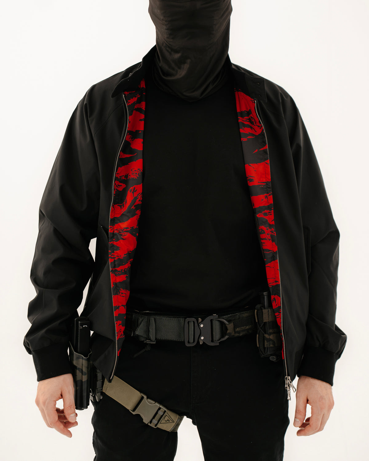 The Pariah Harrington Jacke in Schwarz am Model, Battle Belt mit Beinholster unter der geöffneten Jacke