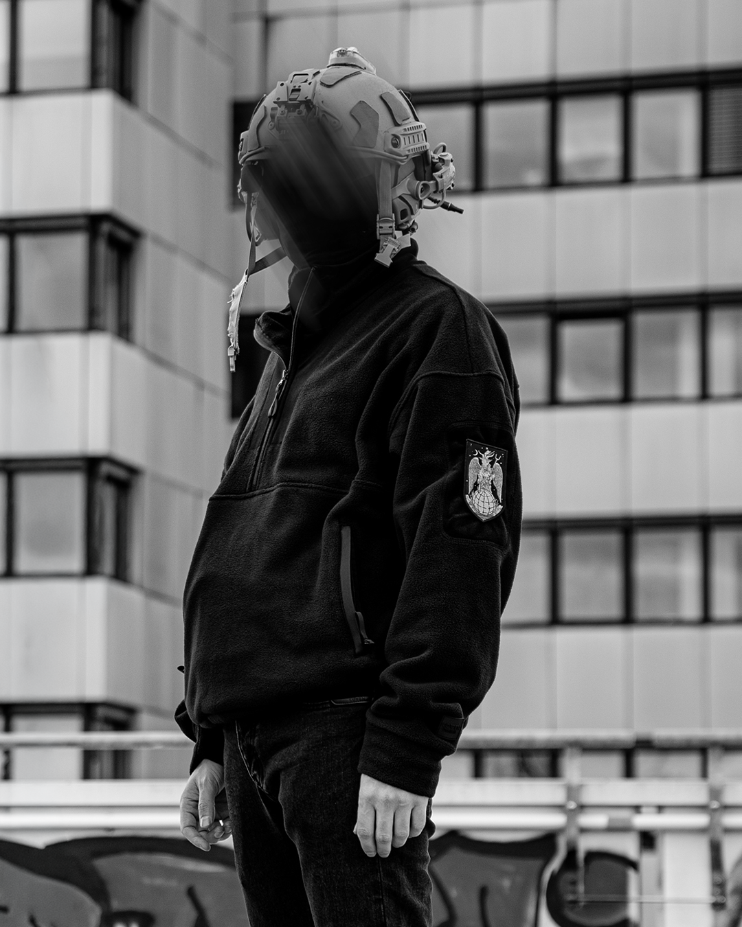 Iscariot 1/2 Zipper Loop Sleeve getragen, Seitenansicht mit taktischem Helm vor Betonfassade