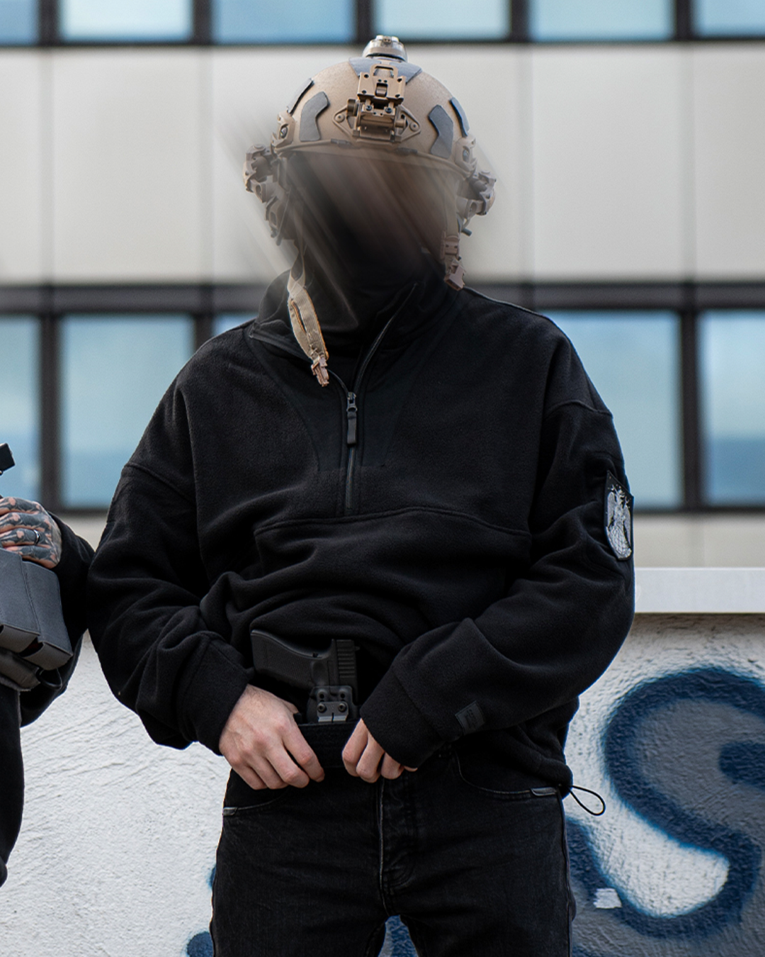 Iscariot 1/2 Zipper Loop Sleeve getragen, Frontalansicht mit taktischem Helm vor Graffitiwand
